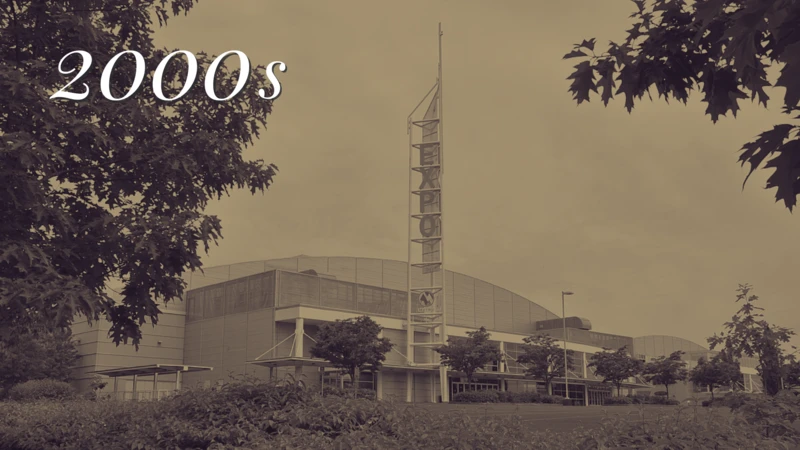 A sepia-toned view of the front of a modern building with trees, and a large "ladder" style sign monument that vertically says "Expo" in neon.