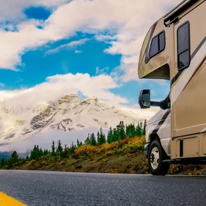 Image of RV driving down the road with clouds and a mountain in the background.