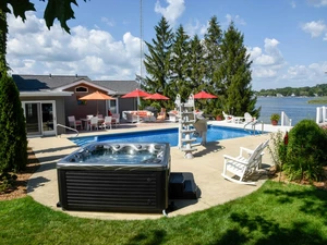 Outdoor hot tub near a outdoor pool and house on a lake. 