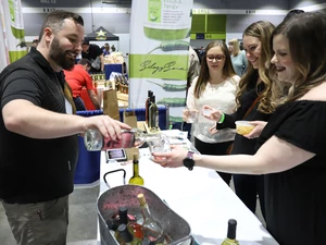 Three girls being poured a sample of wine from a man standing in a booth at the seafood & wine festival