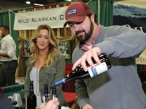 two people working a booth at the seafood & wine festival. One person is pouring wine into a glass.