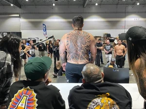 A photo from the portland tattoo expo with two judges looking at a large tattoo on a persons back during a judging.