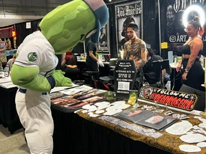 a photo of the pickle mascot looking at a vendor's stickers at the tattoo expo