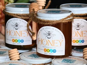 Jars of honey labeled ‘Harvested at Portland Expo Center’ with wooden honey dippers tied on.