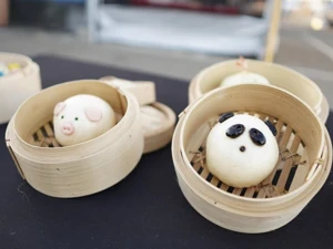 Decorative steamed buns in bamboo baskets on a black table; one bun designed as a pig face and another as a panda face.