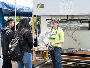 Instructor demonstrates HVAC equipment to two students under a tent.