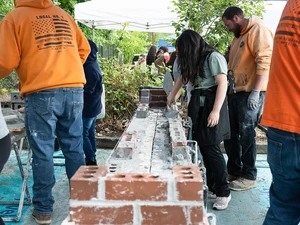 Participants lay bricks during a masonry demonstration with instructors nearby.