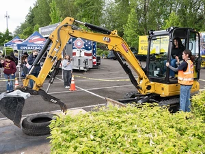 Person operates a small excavator while an instructor guides from outside the cab.