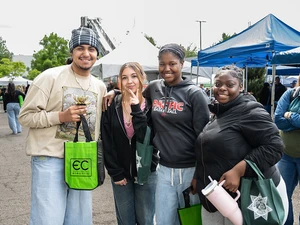 Group of four attendees pose together holding event tote bags outdoors.
